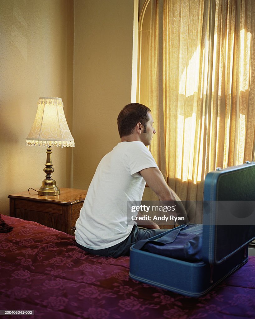 Man sitting on hotel bed by open suitcase