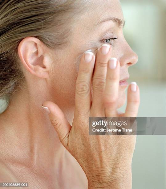 mature woman putting cream on face, side view, close-up - putting lotion stock pictures, royalty-free photos & images