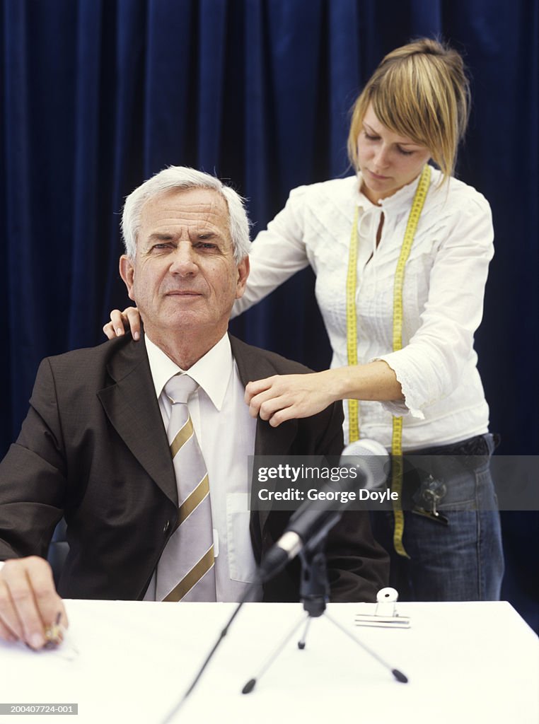 Young woman with measuring tape adjusting jacket of senior man