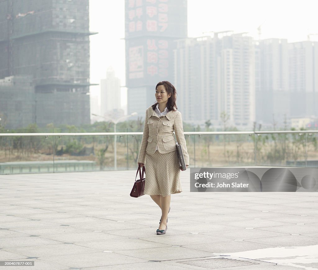 Businesswoman walking across rooftop carrying bag and laptop