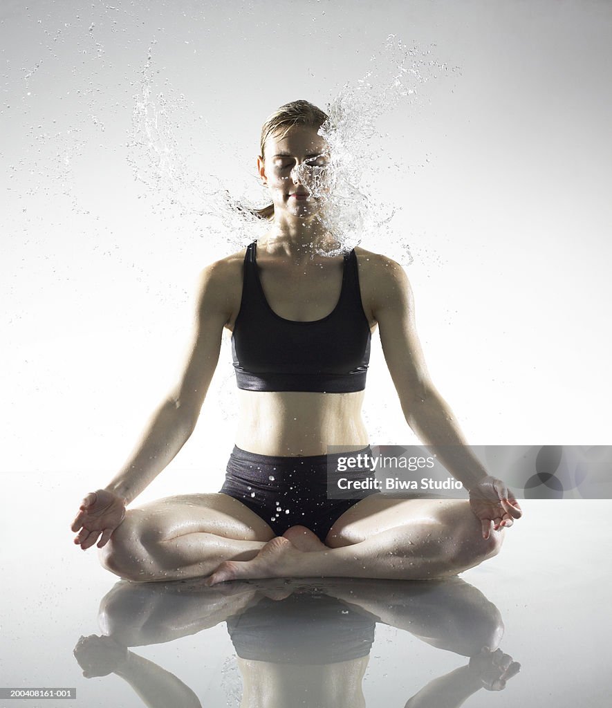 Young woman meditating being splashed with water