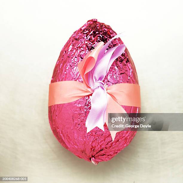 chocolate easter egg wrapped in pink foil and ribbon, close-up - foil foto e immagini stock