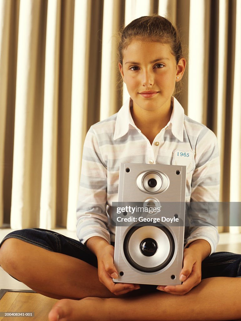 Girl (9-11) sitting cross-legged holding speaker, portrait