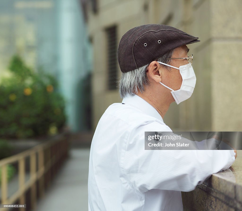 Man wearing pollution mask, leaning on wall, side view