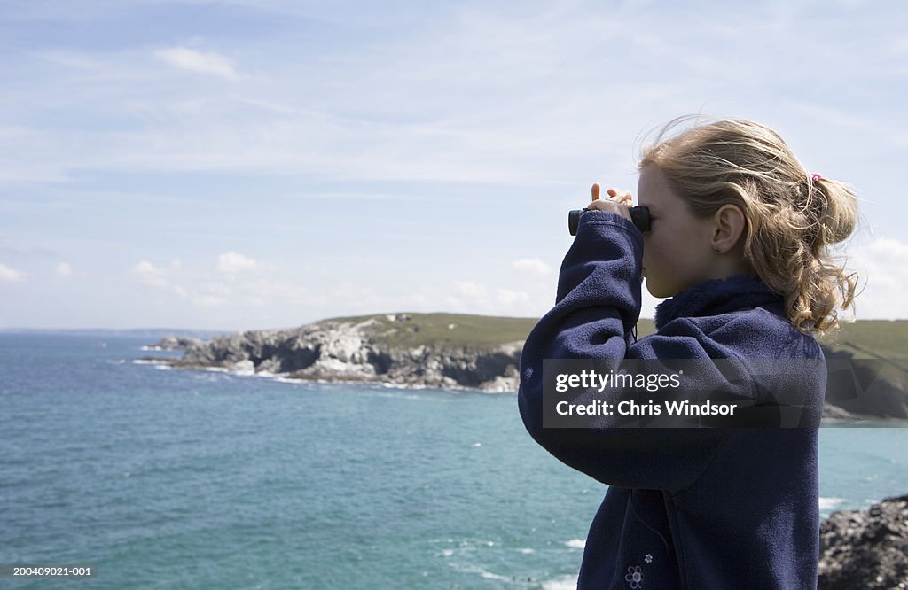 Girl (8-10) looking out to sea through binoculars, side view, close-up