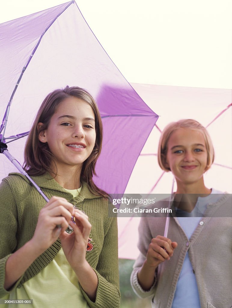 Two girls (11-13) holding umbrellas, smiling, portrait