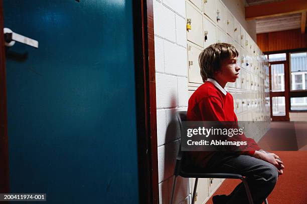 schoolboy (11-13) sitting on chair in corridor, side view - straffen stockfoto's en -beelden