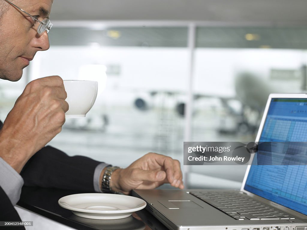 Businessman using laptop whilst drinking from cup, profile, close-up