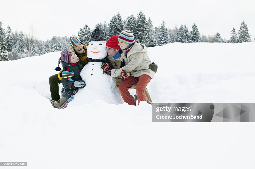 Parents and children (9-13) either side of snowman, boy poking tongue