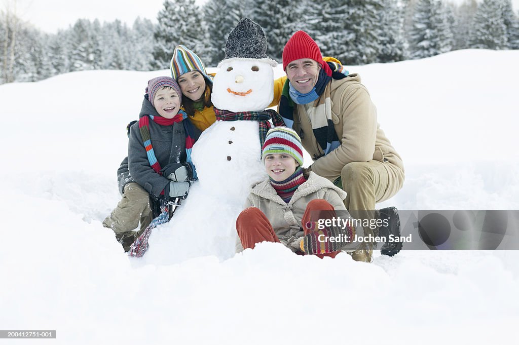 Parents and children (9-13) either side of snowman, smiling, portrait