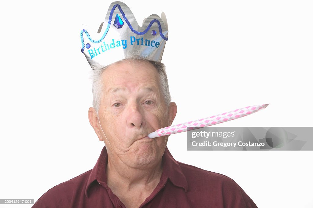 Senior man blowing noisemaker, wearing party hat