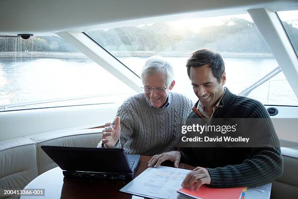 senior und älterer mann sitzt auf yacht mit laptop und lächeln - father son business stock-fotos und bilder