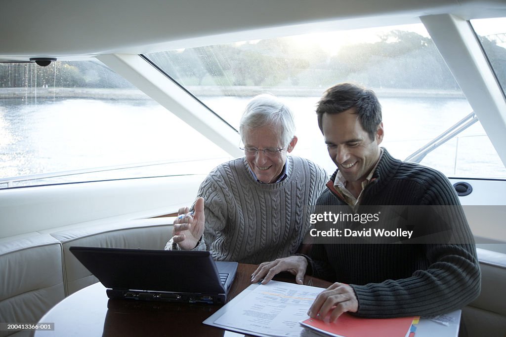 Senior and mature man sitting on yacht using laptop, smiling