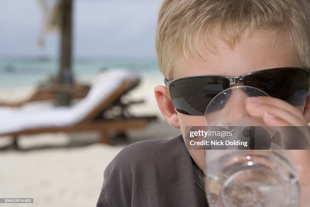 Boy (7-9) wearing sunglasses drinking glass of water on beach