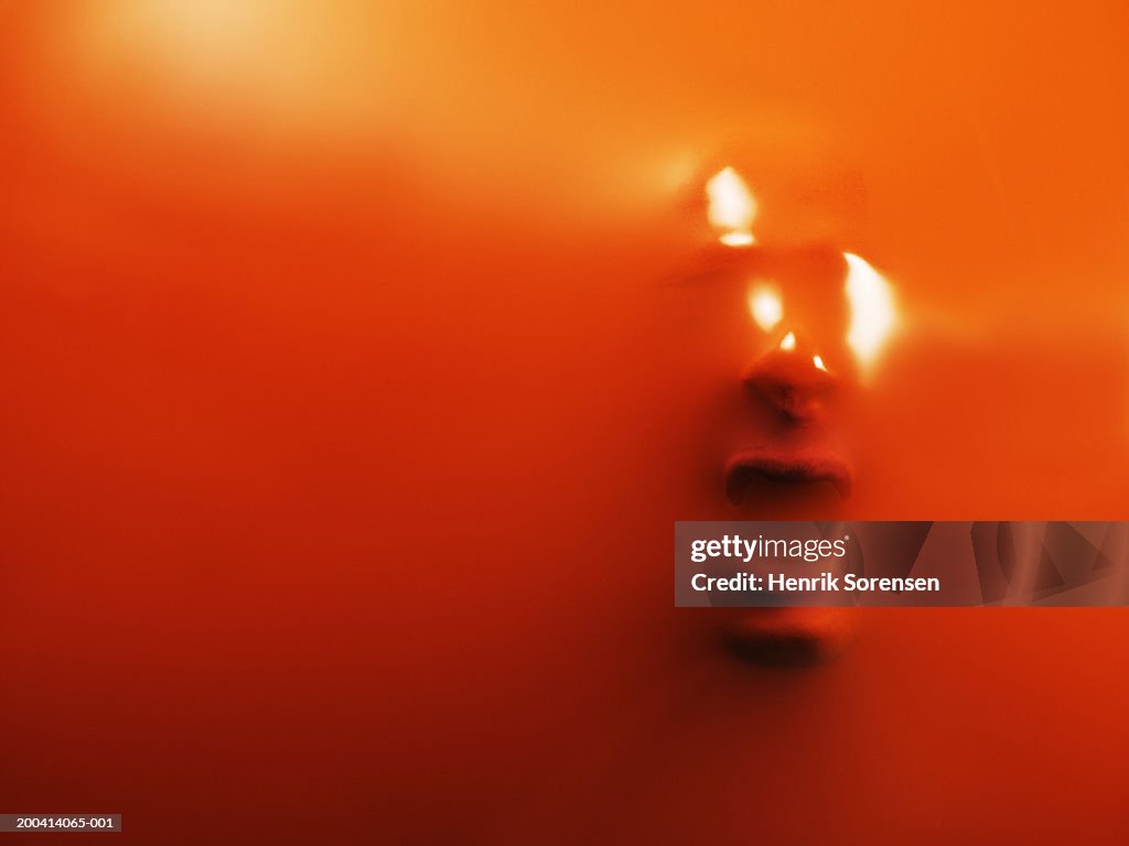 Impression of man's face through orange rubber, close-up