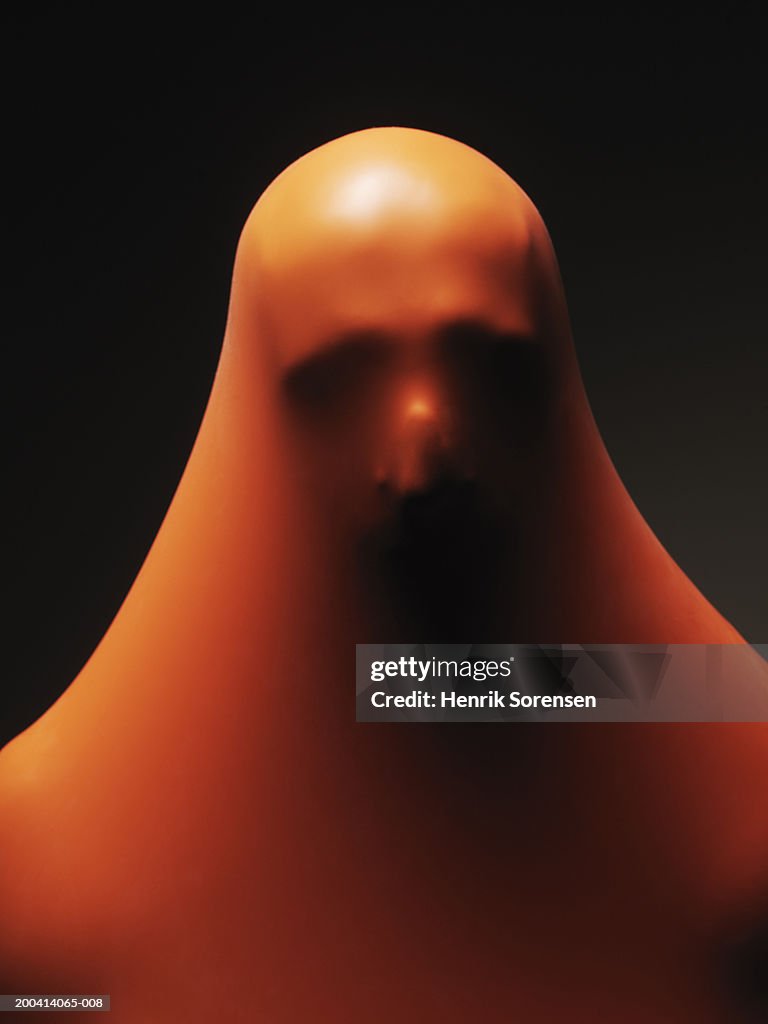 Impression of man's head through orange rubber, close-up