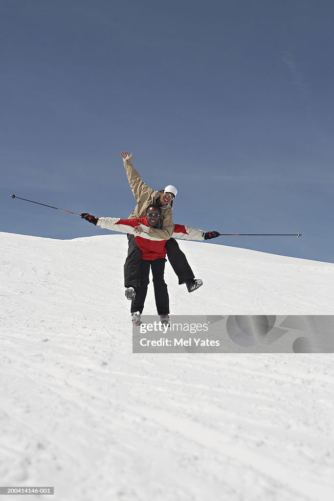 Male skier giving man piggy back on snow covered slope, smiling