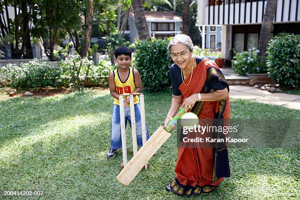 grandmother playing cricket with grandson (6-8) batting ball, smiling - cricket player stock photos et images de collection