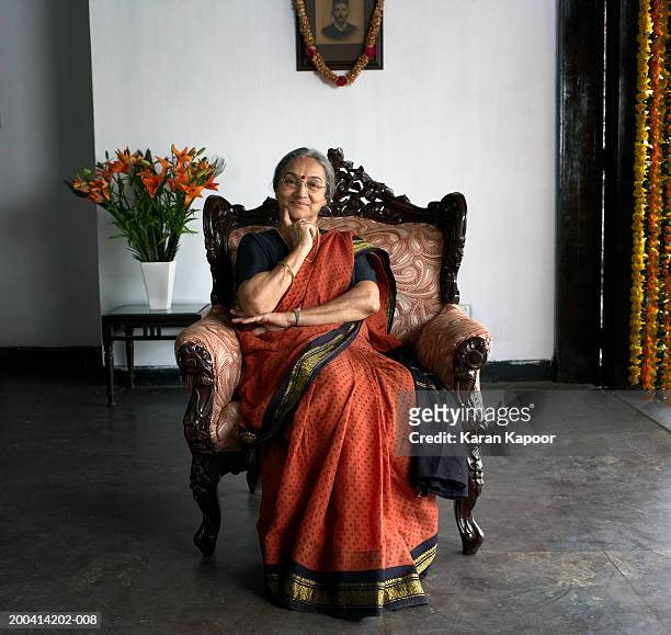 senior woman wearing sari sitting in armchair smiling, portrait - woman thinking hand on chin stock pictures, royalty-free photos & images