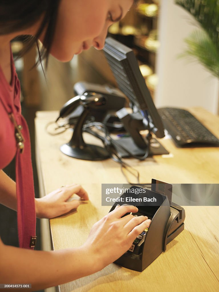 Young woman entering pin number into machine at counter, smiling