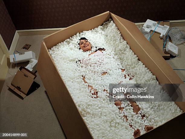 young woman lying in carton covered with packing insulation, elevated - protection humour stock-fotos und bilder