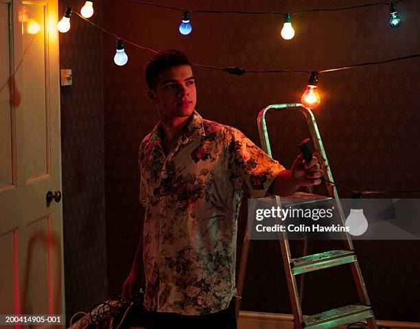 young man in bare room holding cable attached to party lights - clothes on clothes off photos 個照片及圖片檔