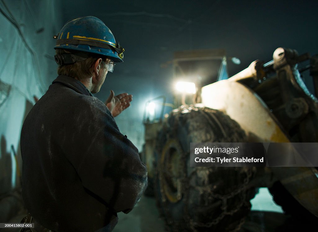 Miner in hardhat signalling to bucket loader in marble quarry