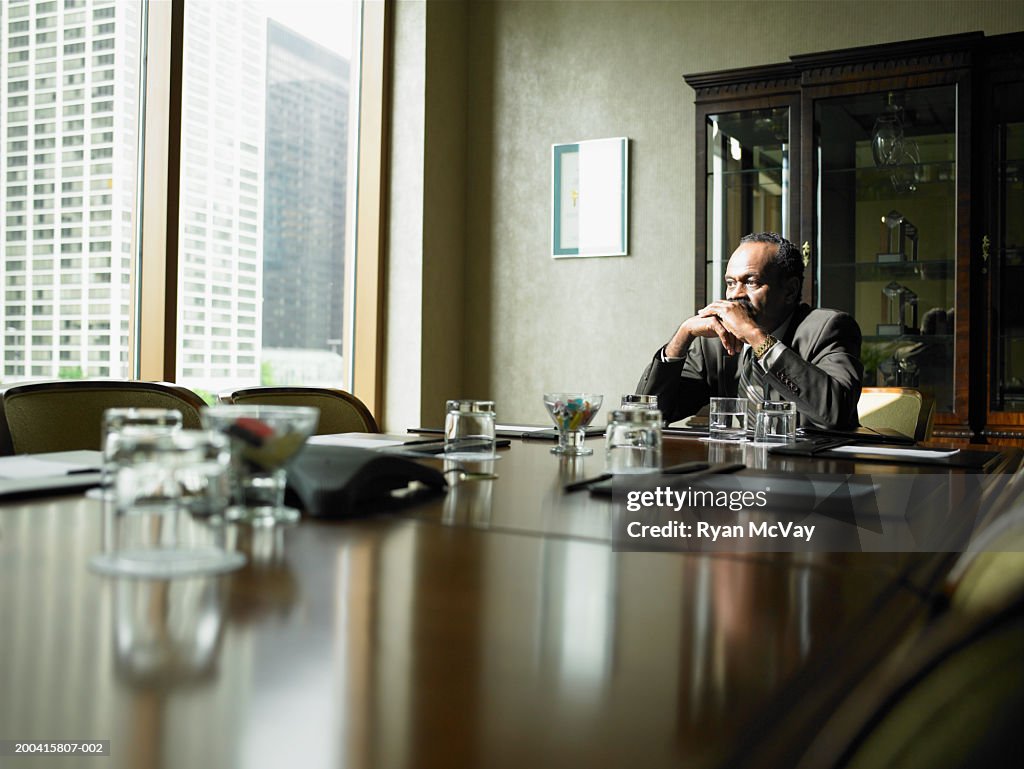 Mature businessman sitting at conference room table, looking pensive