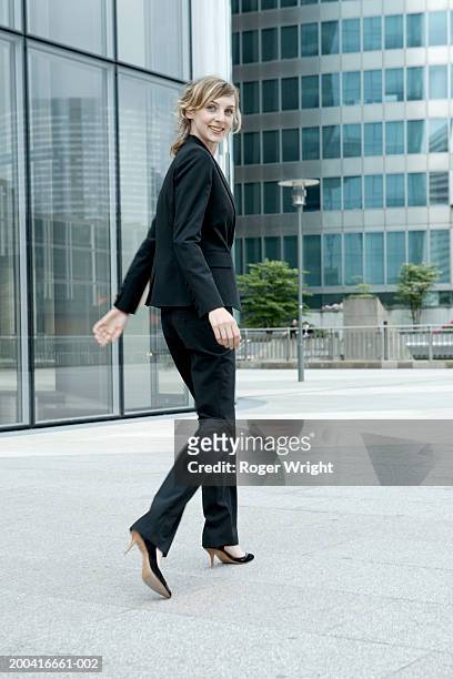 young woman walking along street, looking back over shoulder, smiling - business shoes stockfoto's en -beelden