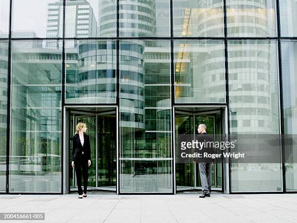 young man entering building as young woman exits - modern office building entrance stock pictures, royalty-free photos & images