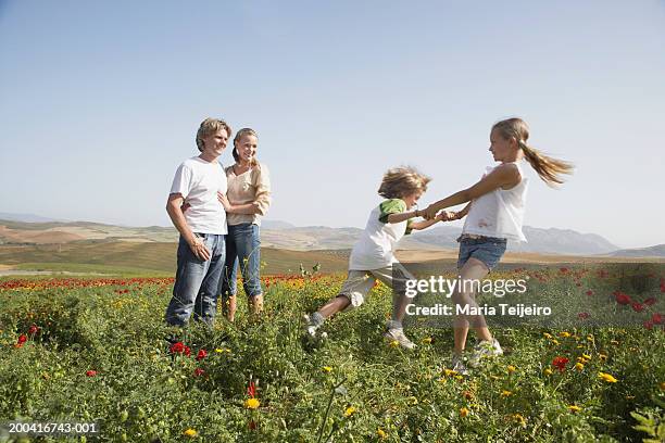 couple watching son and daughter (9-11) swinging each other around - stehmohn stock-fotos und bilder