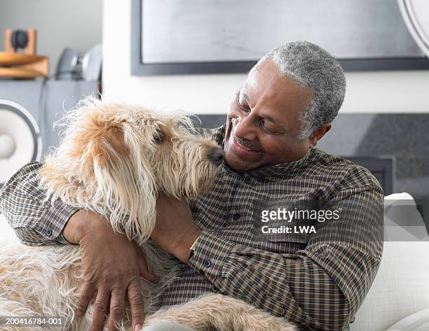 senior man sitting on sofa, playing with dog, close-up - hairy man stockfoto's en -beelden