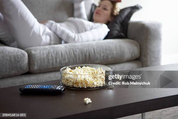 woman lying on sofa (focus on popcorn and remote control on table) - 茶几 個照片及圖片檔