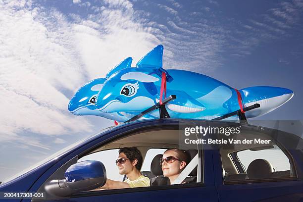 young couple in car, two inflatable dolphins on roof of car - aufblasbarer gegenstand stock-fotos und bilder