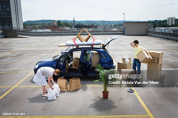 young couple loading boxes and bags into car on rooftop carpark - être à l'arrêt photos et images de collection