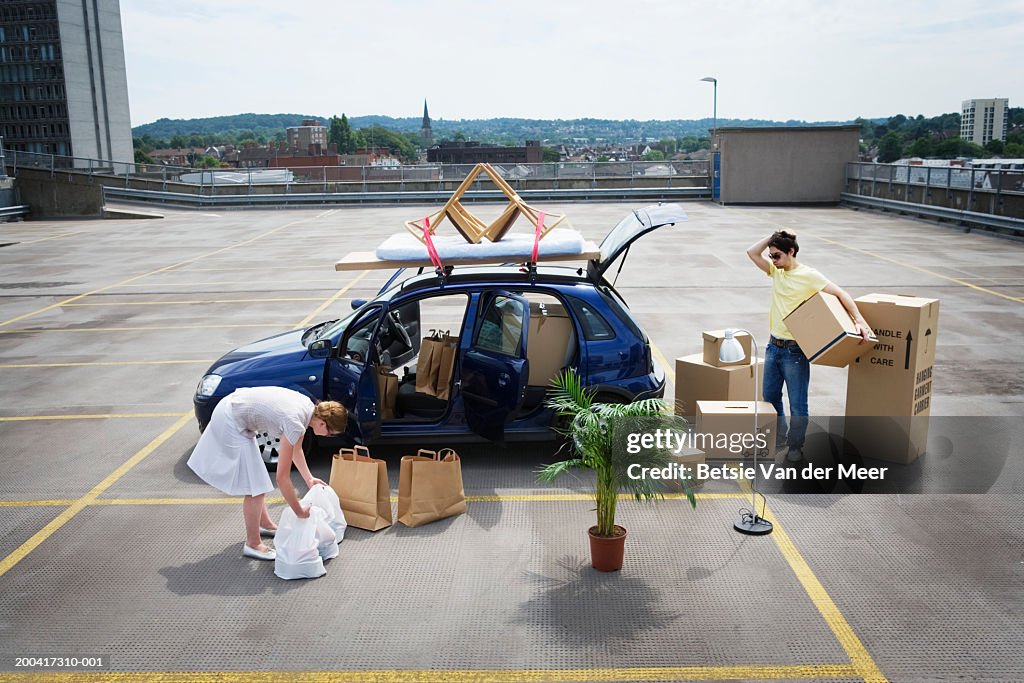 Young couple loading boxes and bags into car on rooftop carpark