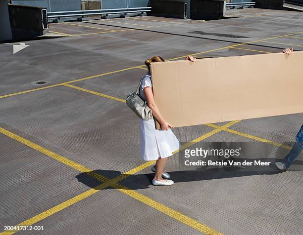 young couple carrying box on rooftop carpark, elevated view - schleppe kleidung stock-fotos und bilder