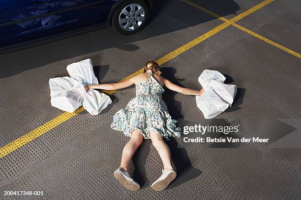 young woman holding shopping bags in carpark, lying face down - lying on front stock pictures, royalty-free photos & images