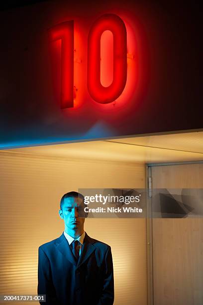 businessman under neon '10' sign, portrait - ten of clubs stock-fotos und bilder