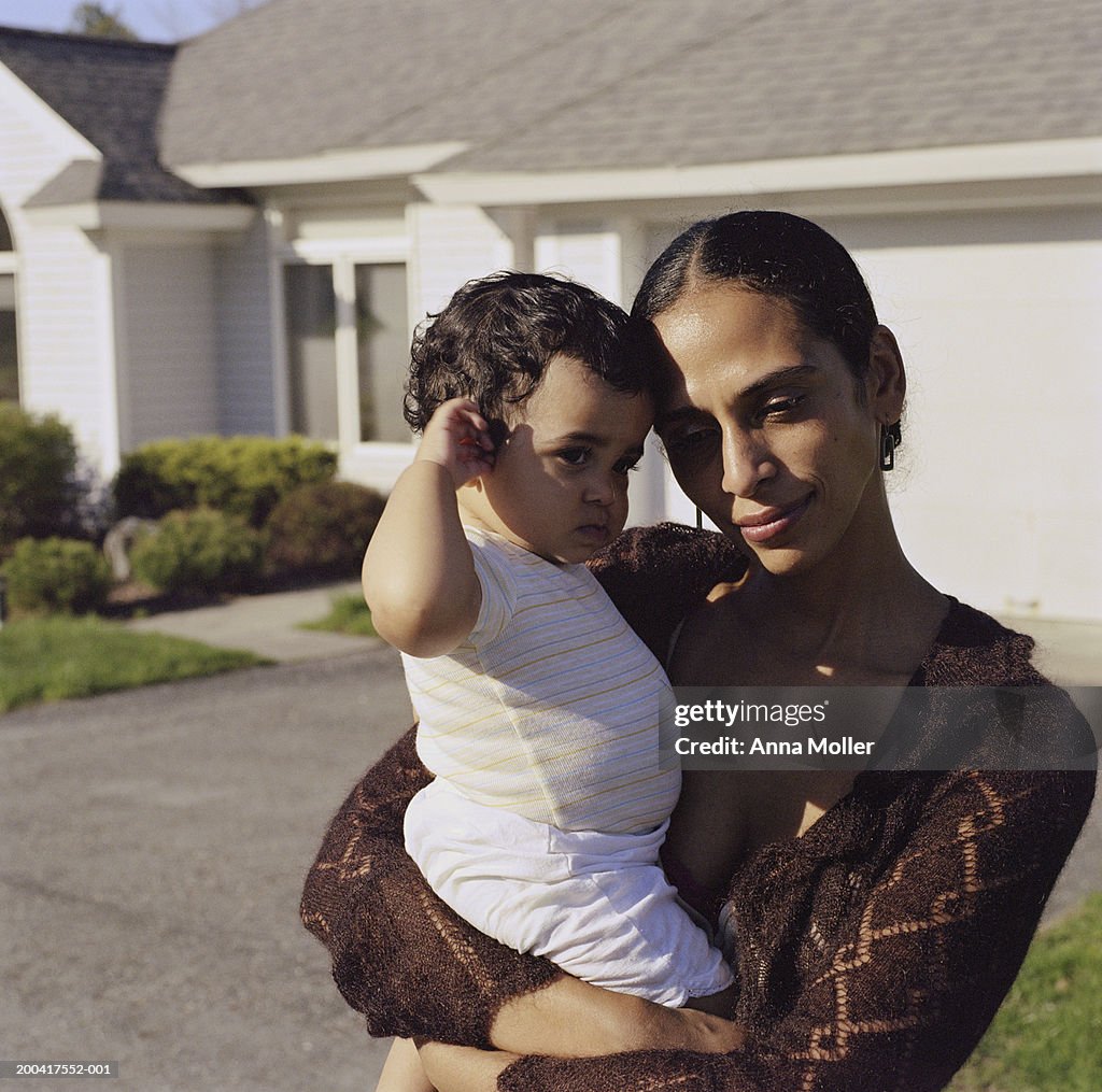 Mother holding daughter (10-12 months) in front of house