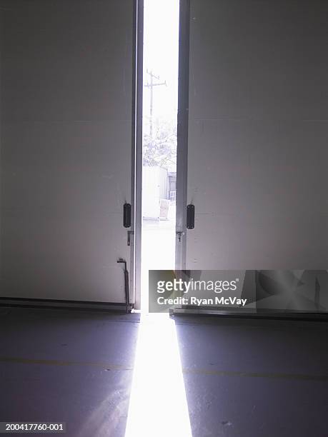 sunlight streaming through partially open warehouse doors - double door stock-fotos und bilder
