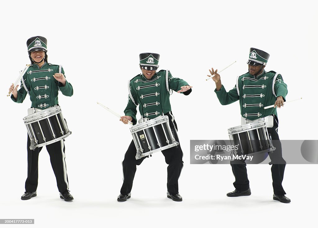 Three teenage boys (14-17) in marching band uniforms playing drums