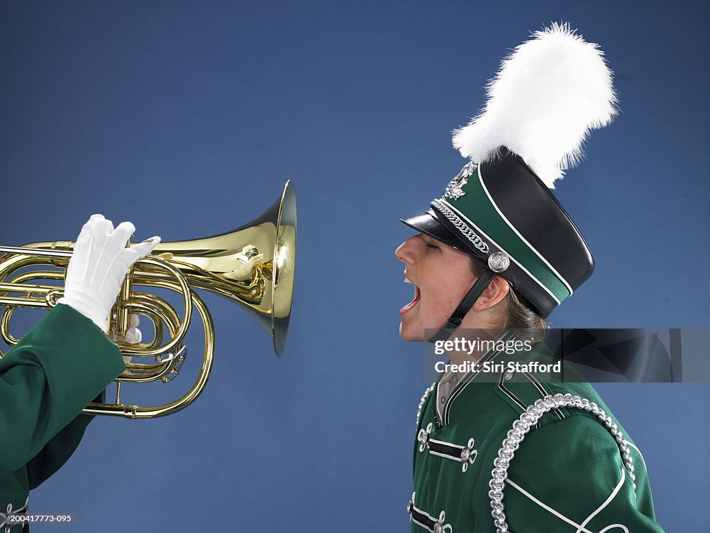 Teenage girl (15-17) in band uniform shouting into horn, side view