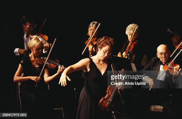 female conductor and violin section performing in orchestra - soliste photos et images de collection