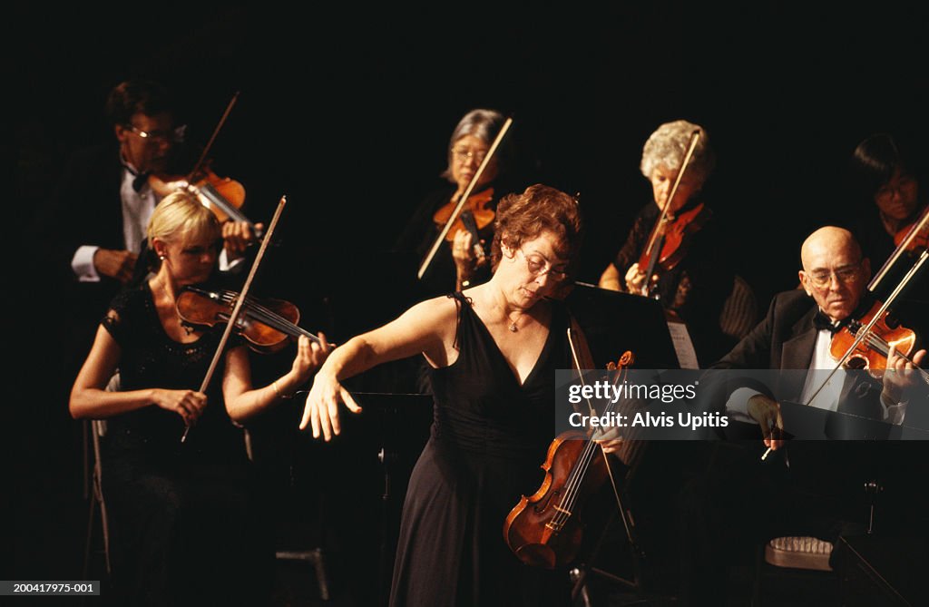 Female conductor and violin section performing in orchestra