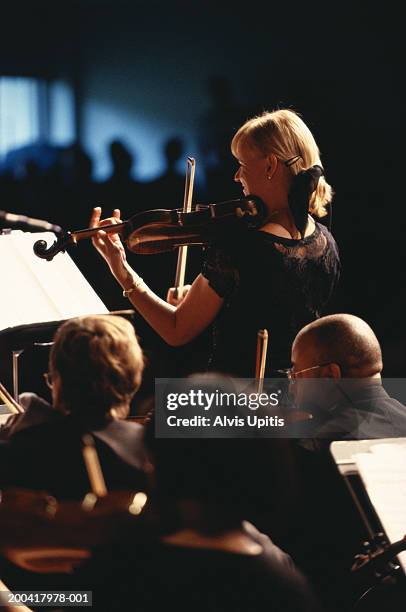 female violin soloist performing in orchestra (focus on woman) - orchestra soloist stock pictures, royalty-free photos & images