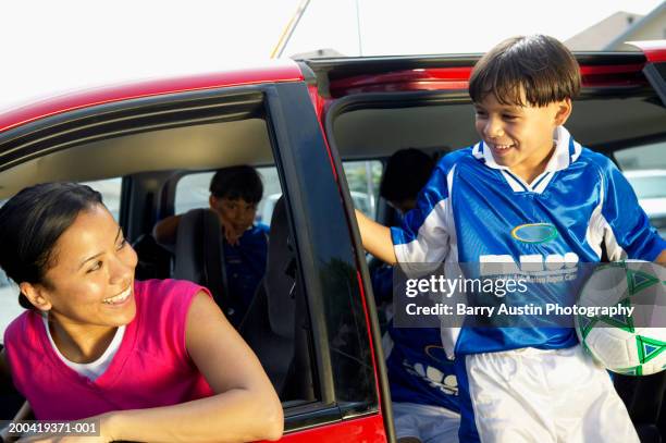 boy (7-9) with football getting out of car, smiling at woman in car - soccer mom stock pictures, royalty-free photos & images