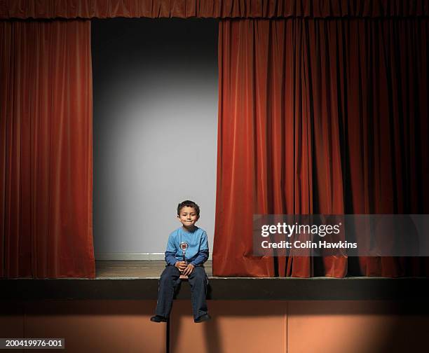 boy (5-7) sitting on edge of stage holding trophy, portrait - theatre awards stock pictures, royalty-free photos & images