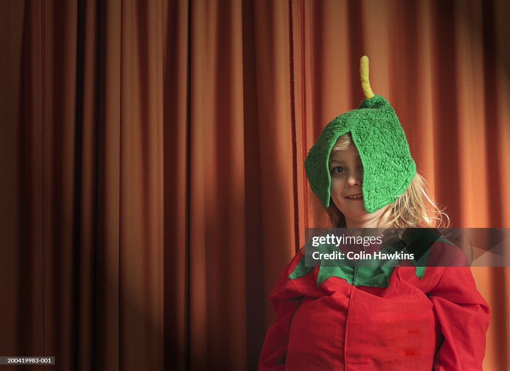 Girl (4-6) by stage curtain wearing tomato costume, portrait, close-up