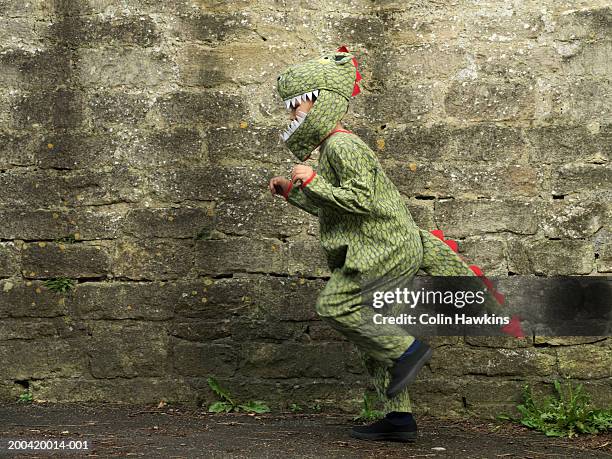 boy (5-7) hopping by brick wall in crocodile costume, side view - costume foto e immagini stock